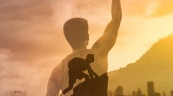 Strong young man in the city with fist in the sky climbing up a mountain.
