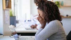 Exhausted African American employee working on project in office. Man and women in casual sitting and standing at table and using laptops. Multiethnic staff concept