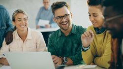 Happy student having fun while using laptop with his friends in