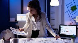 Busy business woman working on financial reports checking numbers for executive meeting. Exhausted manager working with economic statistics at company office late at night