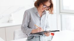 Smiling young woman writing on a clipboard Smiling young woman writing on a clipboard while standing at home