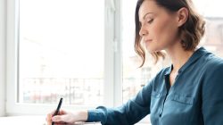 Side view of a young woman making notes in her diary while sitting indoors