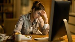 Young displeased woman thinking while working on desktop PC in the evening at home.